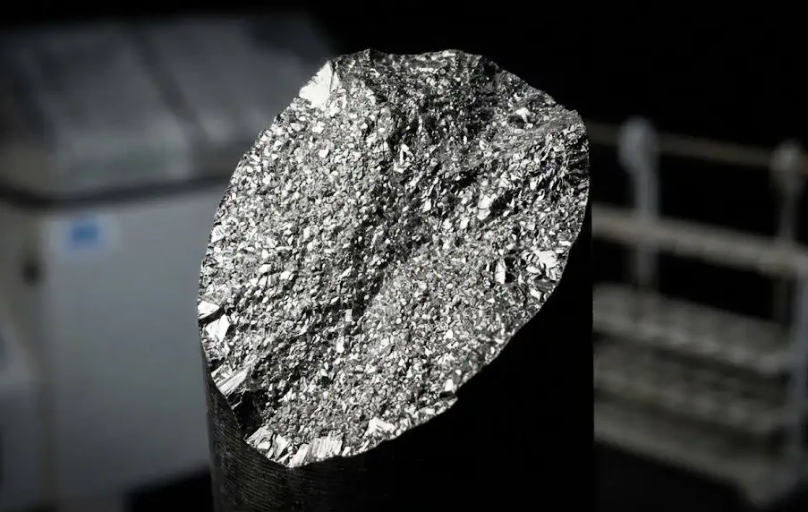 Макрофотография хрупкой, зернистой поверхности излома высокопрочной стальной шпильки, вызванного водородным охрупчиванием, с видимыми в размытом фоне стойкой для гальванического покрытия и камерой солевого тумана.